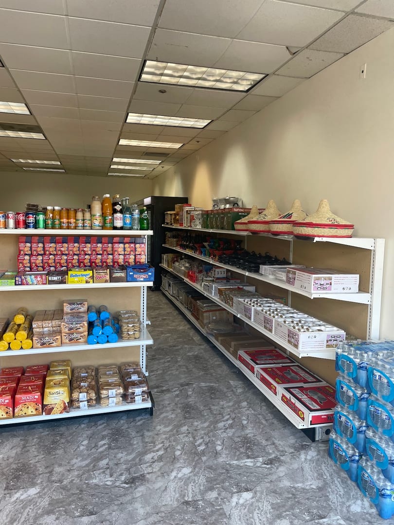 A small grocery store aisle with shelves stocked with drinks, snacks, and household items.