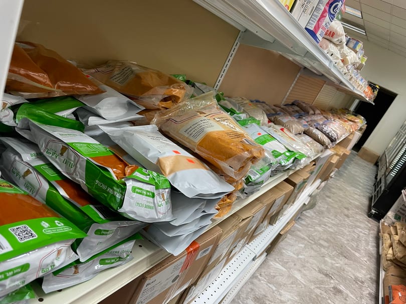Shelves in a grocery store aisle filled with bags of spices, flour, and other packaged goods.