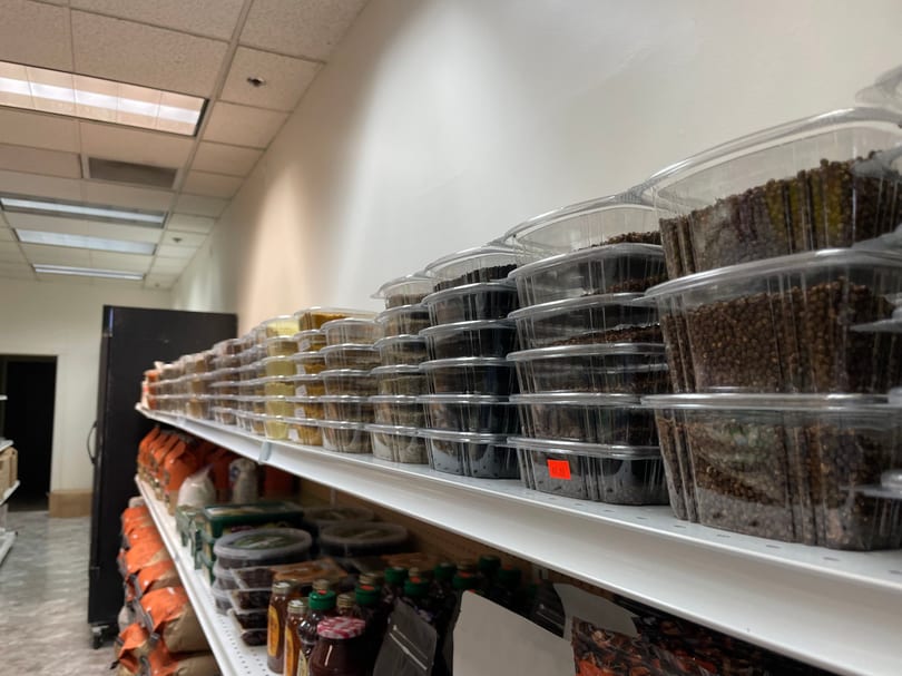 Shelves filled with clear plastic containers of various spices and dried goods in a grocery aisle.