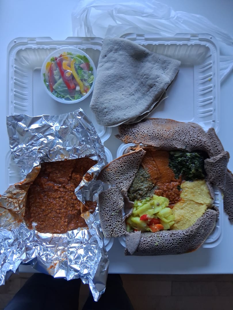 Overhead view of Ethiopian food in takeout containers, including injera, stews, and a side salad.