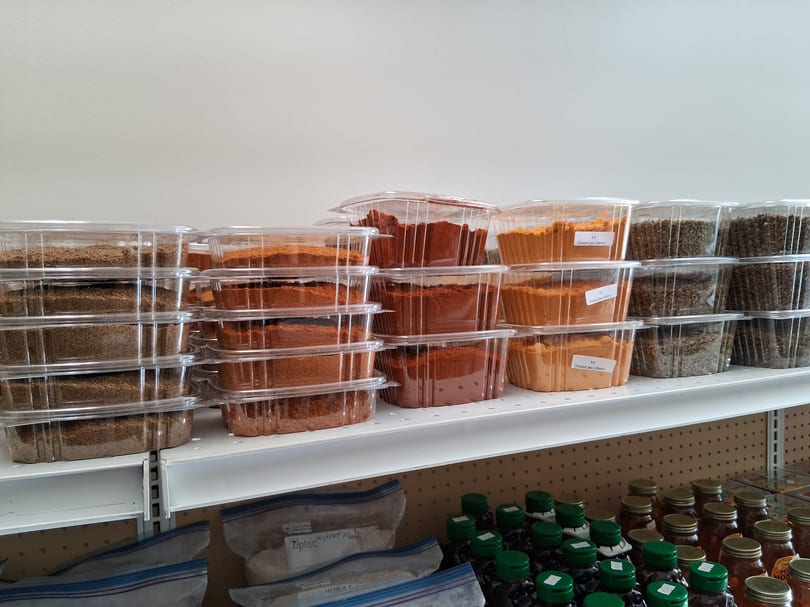 Shelves filled with clear plastic containers of various spices, flours, and bottled goods.